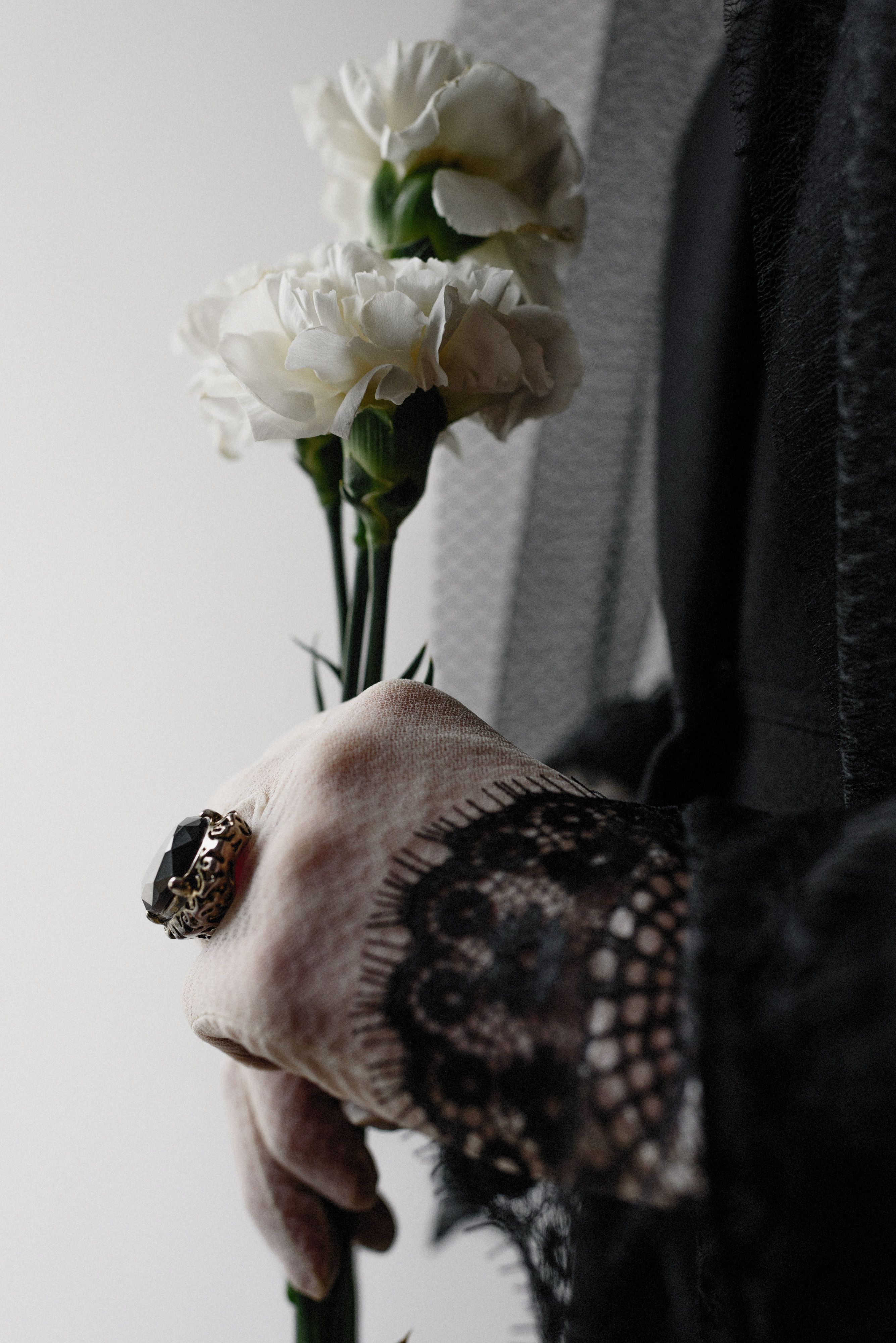 Eine Hand hält zwei weiße Blumen vor dunkler Kleidung
