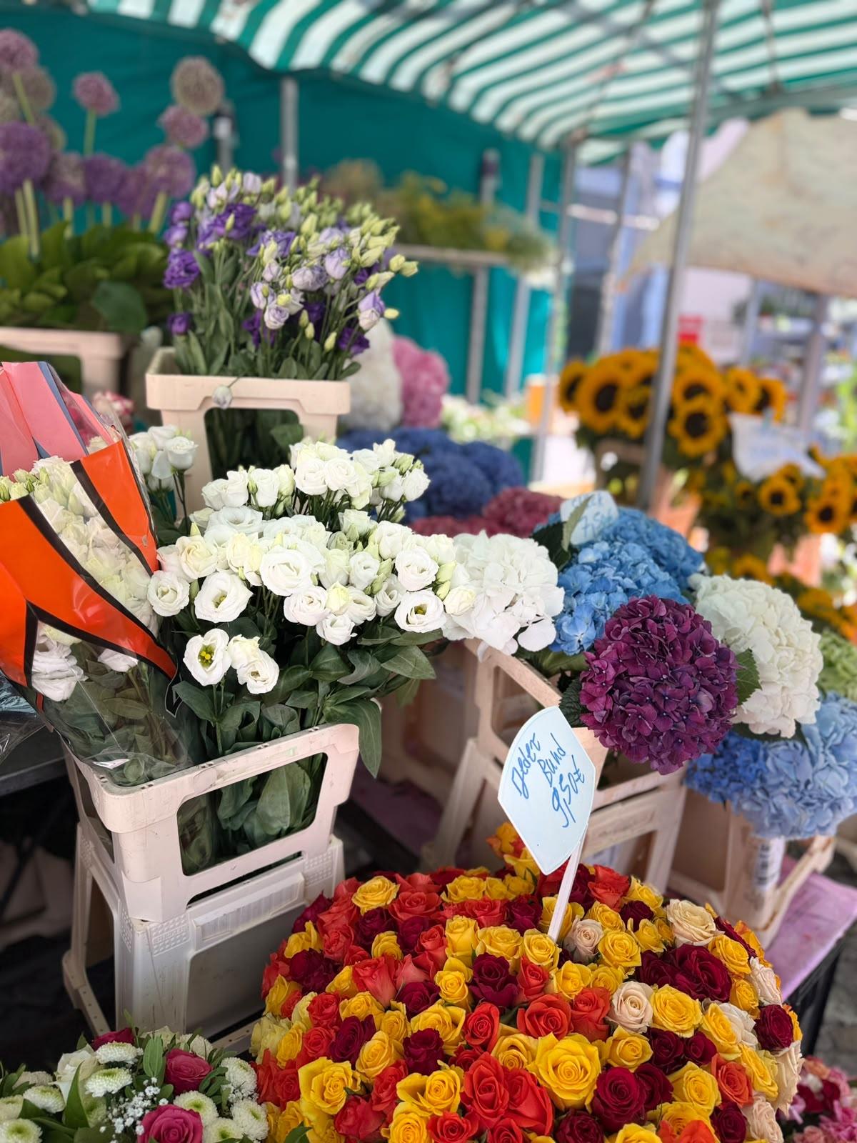 Weiße, gelbe, rote und violette Schnittblumen in Vasen unter einer grün-weiß gestreiften Markise